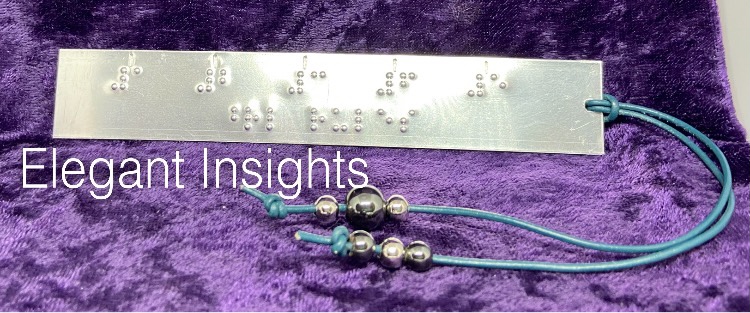 Photo of our "braille rules" aluminum bookmark ruler, shown horizontally, with the cord at right, curving in front to the left.