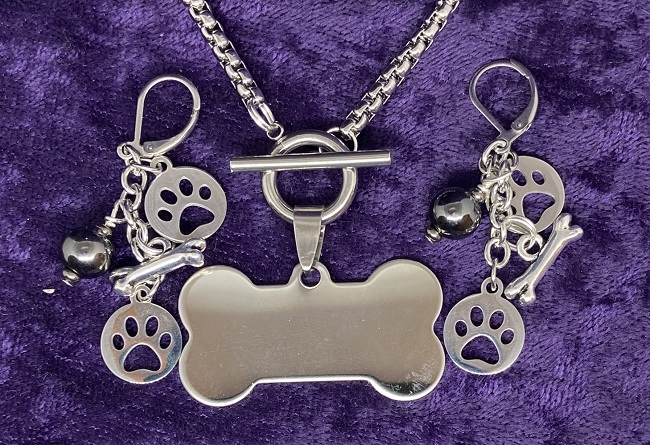 Photo of dog bone necklace, center, with a dangle earring on each side.