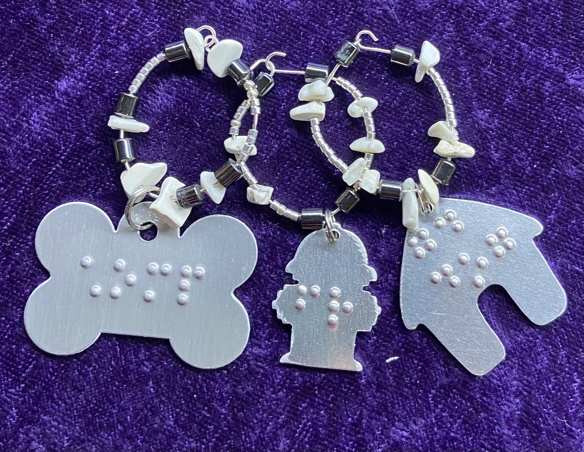 Photo of 3 stemware charms with braille, from left, dog bone, fire hydrant, doghouse.