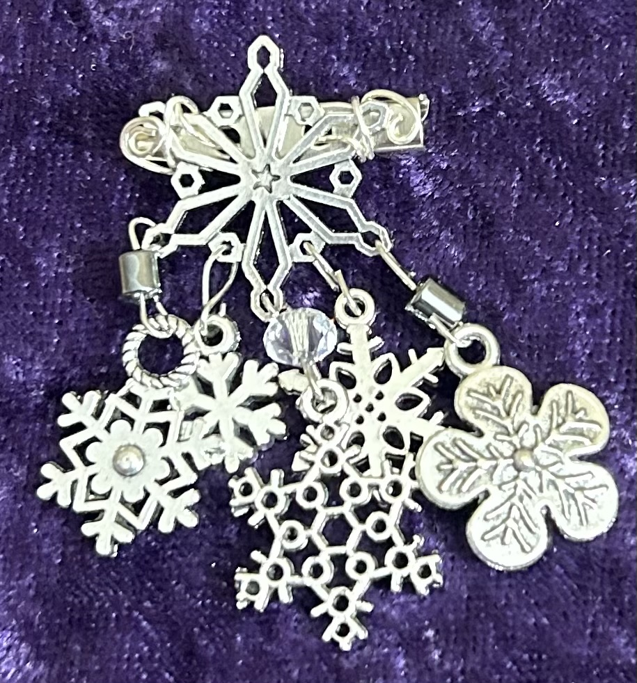 Photo of our Winterscape Snowflake Dangle Pin, with silvery snowflakes dangling from a steel finding embellished with pearl beads and crystals.